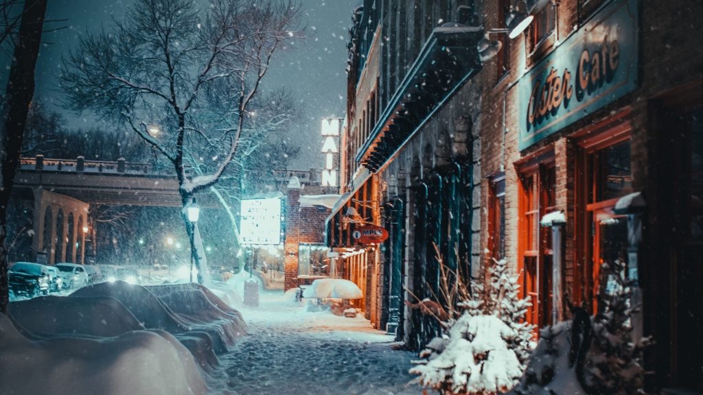 A street covered in snow with red brick buildings down the right.