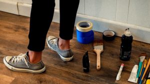 A women's feet wearing grey converse, stood next to DIY tools on the floor.